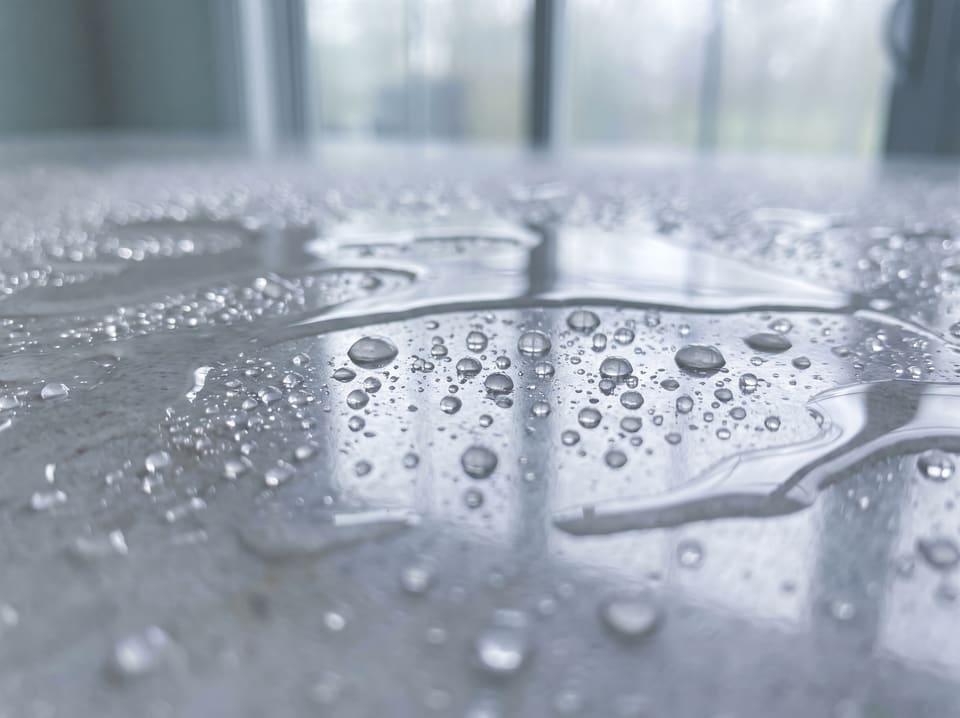 Water beading and sheeting across a polished pale stone countertop.