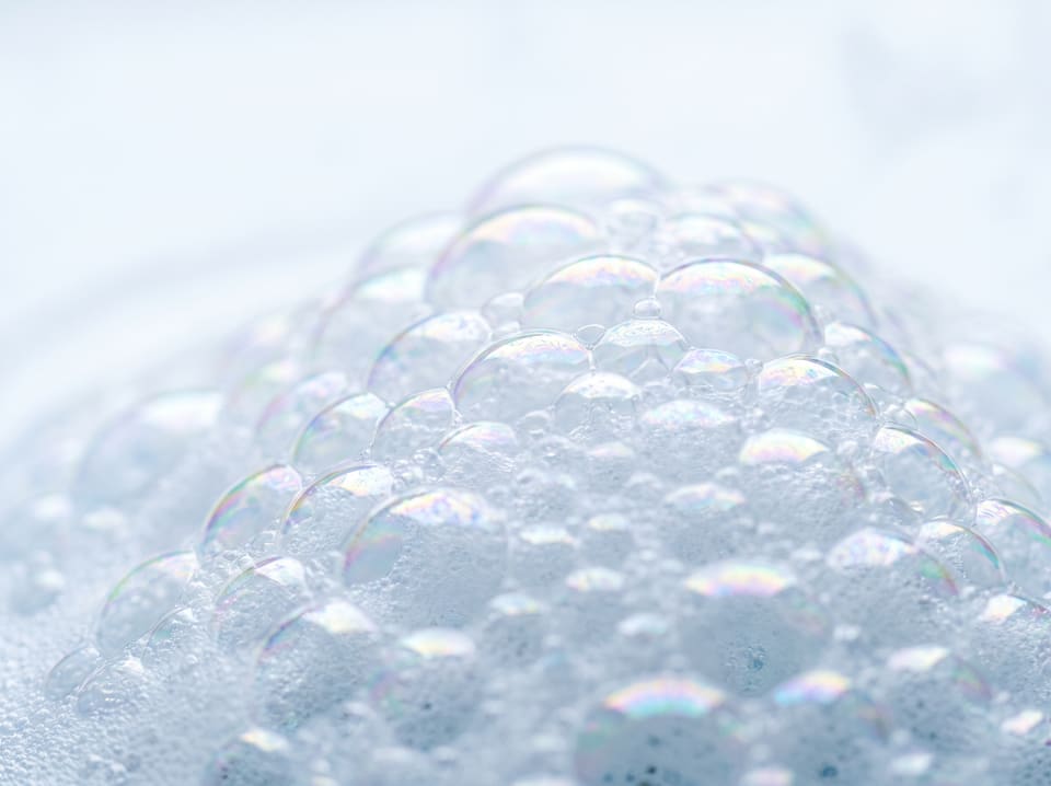 Macro view of fine white soap foam with iridescent highlights on each bubble.