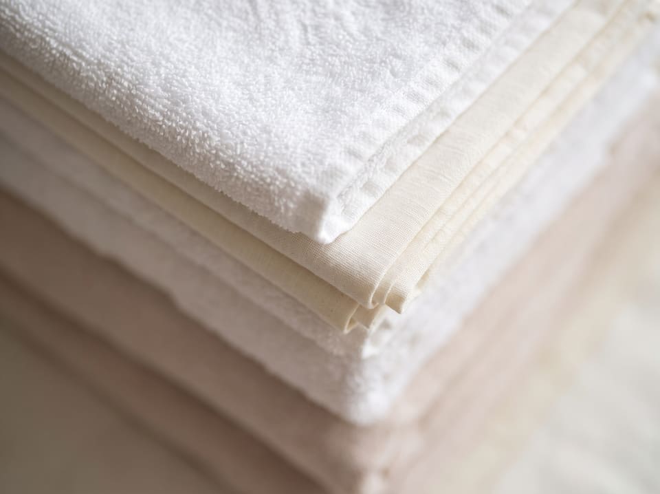 A stack of freshly laundered white towels and folded linen in soft window light.